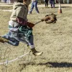 Kid leaping with hobby horse over small hurdle